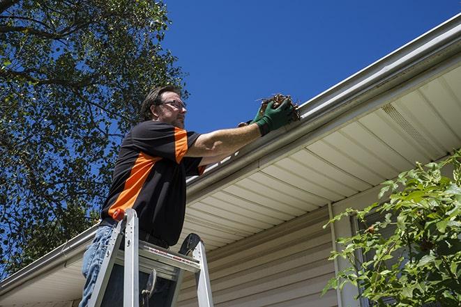 worker repairing damaged gutter on a residential roof in Algona